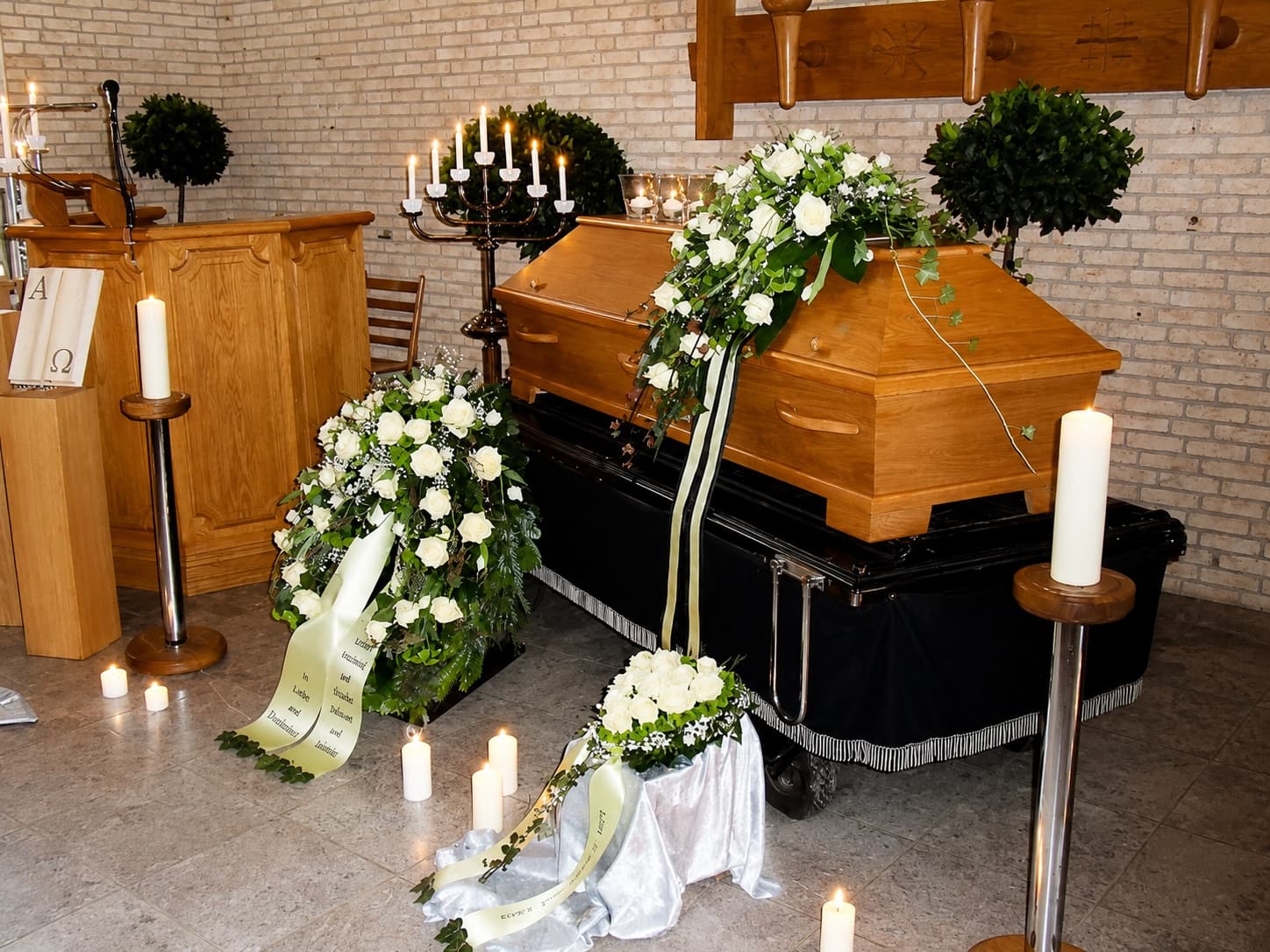 Eichensarg mit weißem Blumenschmuck und Kerzen in einer Trauerhalle