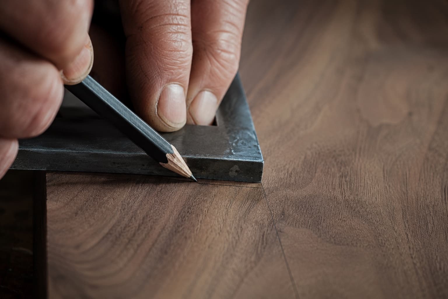 Hand mit Tischlerbleistift und Anschlagwinkel beim Anzeichnen auf einem Stück Holz