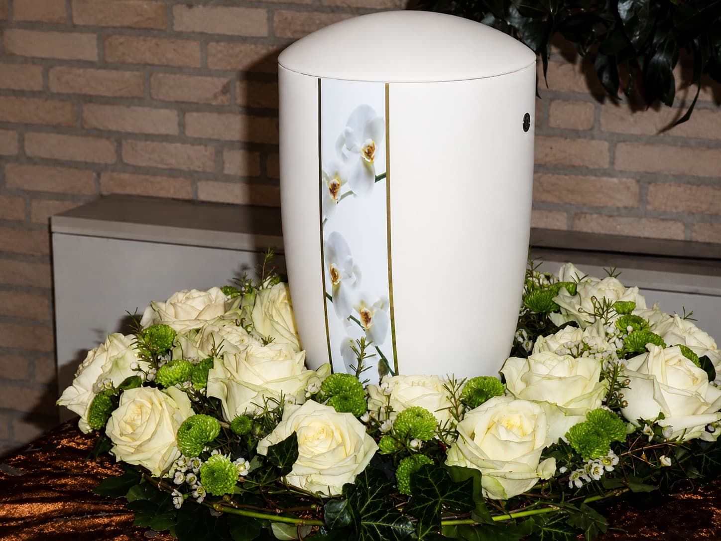 Helle Urne mit Orchideenmotiv, umrahmt von weißen Rosen